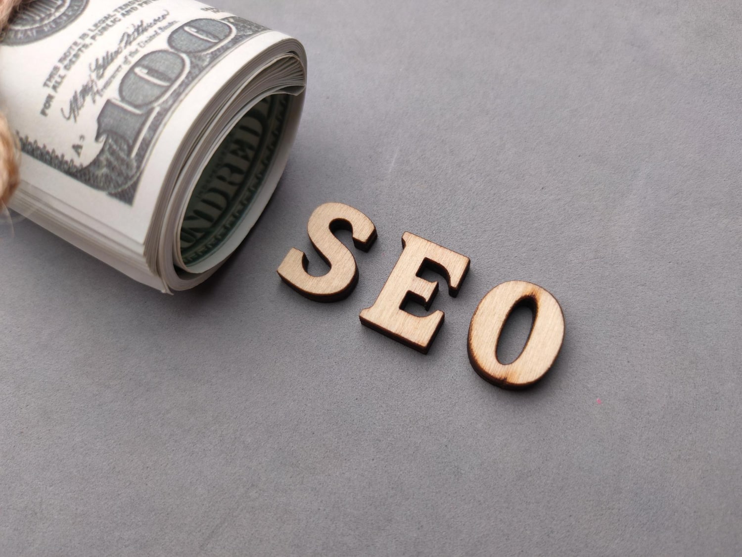 Rolled dollar bills next to wooden letters spelling SEO, symbolizing the cost of search engine optimization.